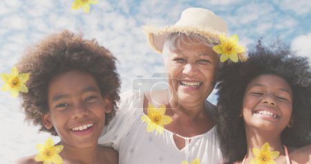 Téléchargez les photos : Image de fleurs sur heureuse femme africaine américaine aînée avec petits-enfants sur une plage ensoleillée. concept de vacances à la plage sain et actif image générée numériquement. - en image libre de droit