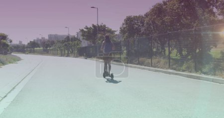 Téléchargez les photos : Spots de lumière contre la vue arrière de la femme afro-américaine en scooter électrique dans la rue. concept de transport écologique - en image libre de droit