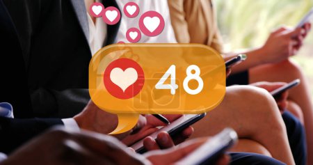 Foto de Imagen digital de un icono del corazón y números crecientes dentro de una caja de chat amarilla. Hay gente con atuendos corporativos sentados en fila mientras revisa sus teléfonos 4k - Imagen libre de derechos