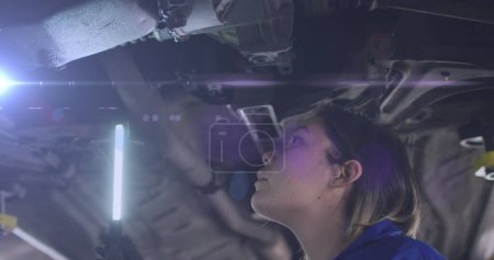 Photo for Image of glowing light over caucasian female car mechanic working in workshop. labor day, work, workers, tradition and celebration concept digitally generated image. - Royalty Free Image