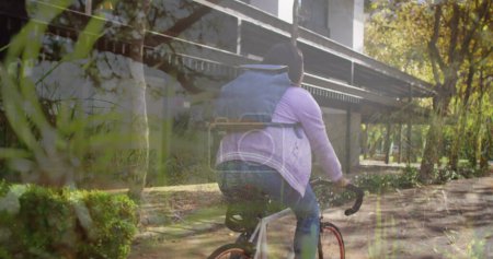 Téléchargez les photos : Image d'arbres sur une femme afro-américaine faisant du vélo. Journée nationale du vélo au travail et concept de célébration image générée numériquement. - en image libre de droit