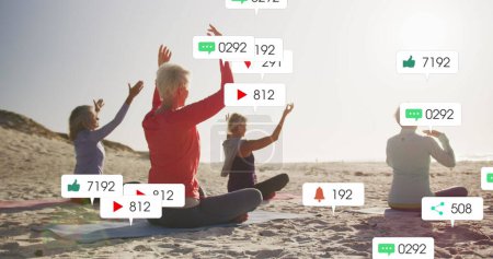 Image of social media notifications, over women doing yoga on beach. positive feelings and wellbeing social media concept, digitally generated image.