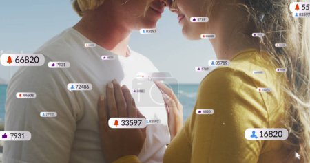 Foto de Imagen de iconos de redes sociales en pancartas sobre parejas caucásicas enamoradas abrazadas por la playa. redes sociales, interfaz digital y concepto de conexiones imagen generada digitalmente. - Imagen libre de derechos