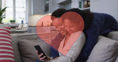 Image of red heart over two woman using smartphone. female power, feminism and gender equality concept digitally generated image.