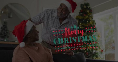 Photo for Image of merry christmas text over senior african american couple wearing santa hats. Christmas, tradition and celebration concept digitally generated image. - Royalty Free Image
