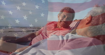 Téléchargez les photos : Image du drapeau des États-Unis d'Amérique sur le couple biracial senior dans des transats sur la plage. Patriotisme américain, diversité et concept de tradition image générée numériquement. - en image libre de droit