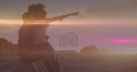 Light trails against african american couple pointing towards a direction sitting on the rocks. Love and relationship concept