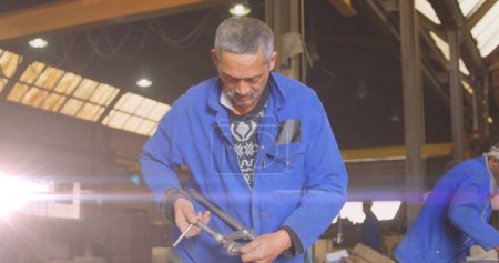 Photo for Image of glowing light over biracial male mechanic in workshop. labor day, work, workers, tradition and celebration concept digitally generated image. - Royalty Free Image