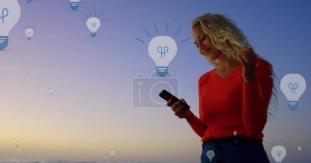 Téléchargez les photos : Image d'icônes d'ampoule au-dessus du milieu de la femme caucasienne à l'aide d'un smartphone au coucher du soleil. connexions mondiales, médias sociaux, technologie et concept d'interface numérique image générée numériquement. - en image libre de droit