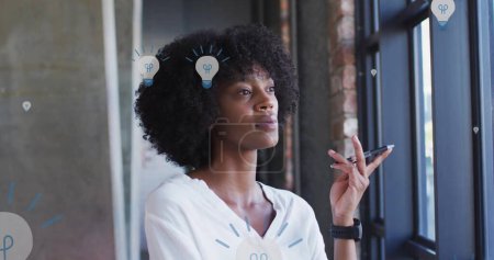 Téléchargez les photos : Image des icônes de l'ampoule sur une femme d'affaires afro-américaine en fonction. Médias sociaux mondiaux, réseaux, interface numérique et concept de traitement des données image générée numériquement. - en image libre de droit