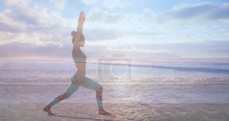 Téléchargez les photos : Vue latérale d'une femme faisant du yoga sur la plage par une journée ensoleillée - en image libre de droit