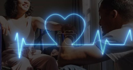 Imagen de ritmo cardíaco de neón y corazón sobre feliz pareja birracial, mujer en silla de ruedas. Imagen generada digitalmente del concepto de monitoreo de funciones de salud y vida.