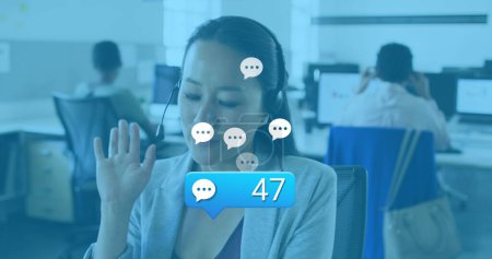 Image of social media reactions over asian woman in office having call. Business, social media, communication and technology concept digitally generated image.