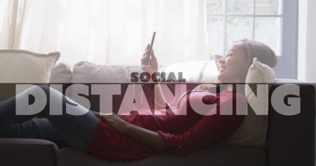 Photo for Image of social distancing text over woman using smartphone at home. global coronavirus pandemic and online connection social media concept digitally generated image. - Royalty Free Image