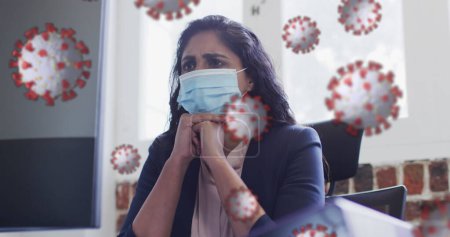 Photo for Image of covid 19 cells floating over worried biracial woman wearing face mask in office. Healthcare and protection during coronavirus covid 19 pandemic, digitally generated image. - Royalty Free Image