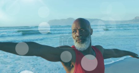 Téléchargez les photos : Image d'un homme afro-américain expérimenté pratiquant le yoga à la plage sur des spots lumineux. concept de loisir et de bien-être image générée numériquement. - en image libre de droit