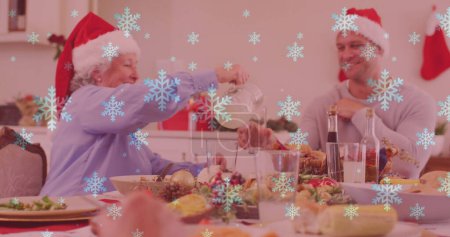 Photo for Image of snow falling over smiling caucasian family with santa hats having dinner. christmas, winter, tradition and celebration concept digitally generated image. - Royalty Free Image