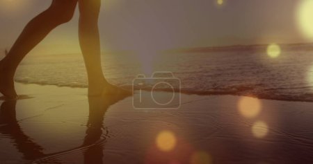 Téléchargez les photos : Des taches jaunes de lumière sur la partie médiane d'une femme marchant sur la plage. Concept d'amour et de relation - en image libre de droit