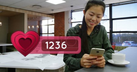 Photo for Close up of an Asian girl in a cafeteria typing on her mobile phone while on a coffee break. In the left corner a digital image of a heart icon with a number count up bar - Royalty Free Image