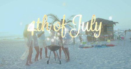 Foto de Grupo de personas celebrando el 4 de julio en una playa. Se reúnen alrededor de una barbacoa, disfrutando del ambiente festivo de las vacaciones.. - Imagen libre de derechos