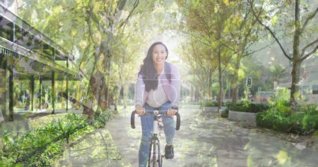 Photo for Image of leaves over smiling asian woman cycling. national bike to work day and celebration concept digitally generated image. - Royalty Free Image