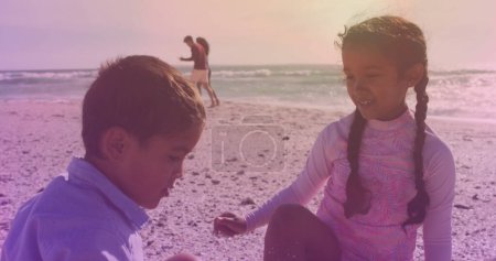 Foto de Spots of light against hispanic brother and sister high fiving each other at the beach. national siblings day awareness concept - Imagen libre de derechos