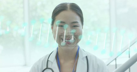 Foto de Imagen de la hebra de ADN sobre el retrato de sonriente médico diverso que trabaja en el hospital. Concepto de servicios médicos y sanitarios imagen generada digitalmente. - Imagen libre de derechos