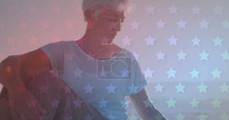 Foto de Senior mujer caucásica con pelo gris se ve contemplativa. Ella está rodeada por un escenario de ensueño con patrones de estrellas, evocando una sensación de nostalgia. - Imagen libre de derechos