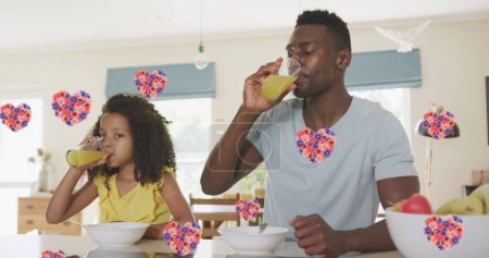 Photo for Image of flower hearts over african american father and daughter drinking juice at home. family life, love and care concept digitally generated image. - Royalty Free Image