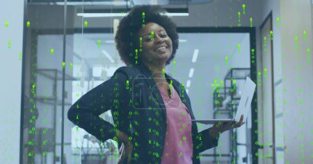 Bild der gelben Datenverarbeitung über der afrikanisch-amerikanischen Geschäftsfrau mit dem Laptop im Büro. Daten, Netzwerke, digitale Schnittstelle, Wirtschaft und Kommunikation, digital erzeugtes Bild.