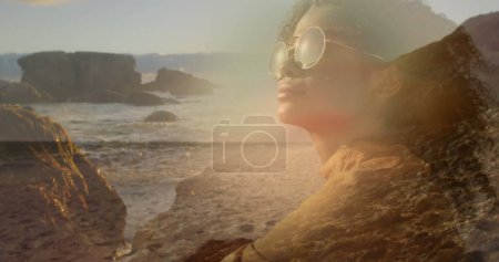 Photo for Image of african american woman in sunglasses over sunny landscape. happy holidays and free time, digitally generated image. - Royalty Free Image