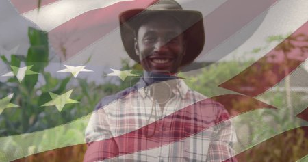 Image of flag of united states of america over african american farmer in hat. american patriotism and independence concept digitally generated image.