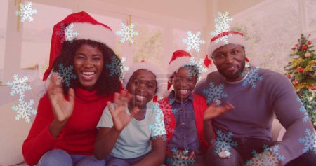 Téléchargez les photos : Image de neige tombant sur une famille souriante avec des chapeaux de Père Noël agitant les mains. Noël, hiver, tradition et concept de célébration image générée numériquement. - en image libre de droit