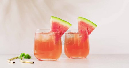 Photo for Two glasses of watermelon juice are on display, with copy space. Refreshing summer drinks with a slice of watermelon add a vibrant touch to the setting. - Royalty Free Image