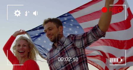 Foto de Imagen de una pareja caucásica corriendo con una bandera americana, vista en una pantalla de una cámara digital en modo de grabación con iconos y temporizador - Imagen libre de derechos