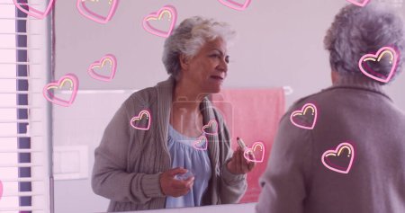 Téléchargez les photos : Image de cœurs roses sur heureuse femme âgée caucasienne portant du rouge à lèvres à la maison. retraite style de vie et concept de bien-être image générée numériquement. - en image libre de droit