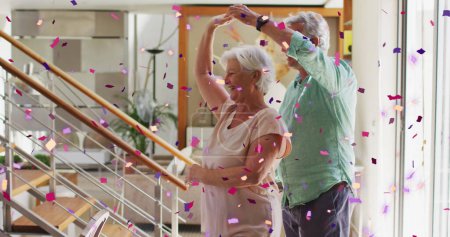 Image of pink and purple confetti falling over happy caucasian senior couple dancing at home. retirement lifestyle, romance and celebration concept digitally generated image.