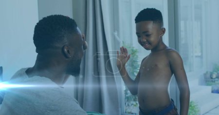 Photo for Image of lights over happy african american father and son undressing and clapping hands. family, togetherness, spending quality time concept digitally generated image. - Royalty Free Image