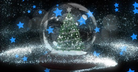 Téléchargez les photos : Étoile filante au-dessus du sapin de Noël dans une boule à neige contre plusieurs étoiles bleues flottant. Noël fête et concept de célébration - en image libre de droit