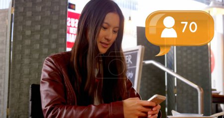 Foto de Primer plano de la hermosa mujer asiática escribiendo en el teléfono móvil mientras está sentado en el restaurante. Imagen digital de la burbuja de mensajes con el icono del seguidor y el recuento de números - Imagen libre de derechos