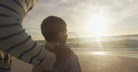 Foto de Un niño birracial disfruta de una puesta de sol en la playa, con espacio para copiar. El ambiente sereno al aire libre crea un momento de paz para la reflexión. - Imagen libre de derechos