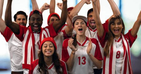 Foto de Vista frontal de un grupo de aficionados al deporte con camisetas rojas y blancas animando en voz alta - Imagen libre de derechos