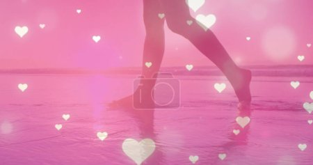 Téléchargez les photos : Icônes de coeur éclatantes multiples tombant contre la section basse d'une femme marchant sur la plage. Concept d'amour et de relation - en image libre de droit