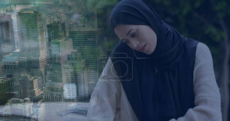 Photo for Image of ssian woman in hijab using smartphone over cityscape. communication technology and keeping in touch. digitally generated image. - Royalty Free Image