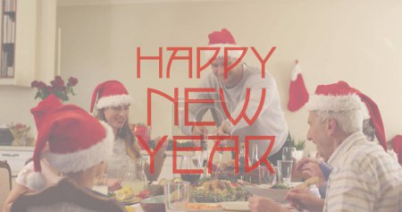 Image of happy new year text in red over family in santa hats at dinner table. New year, greeting, christmas, family, celebration and tradition concept digitally generated image.