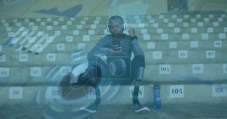 Image of digital data processing over disabled male athlete in stands of sports stadium. global sports, competition, disability and digital interface concept digitally generated image.