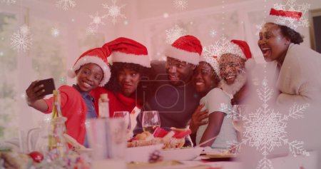 Téléchargez les photos : Image de neige tombant sur une famille souriante avec des chapeaux de Père Noël prenant selfie. Noël, hiver, tradition et concept de célébration image générée numériquement. - en image libre de droit
