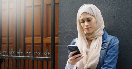 Téléchargez les photos : Image de femme asiatique en hijab avec smartphone sur paysage urbain. technologie de communication et garder le contact, image générée numériquement. - en image libre de droit