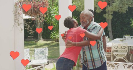 Foto de El hombre birracial mayor abraza a un joven afroamericano. Ambos sonríen, compartiendo un momento de afecto y alegría en un jardín. - Imagen libre de derechos