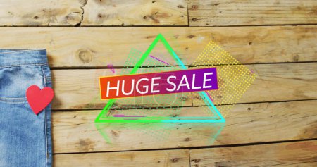 Photo for Image of huge sale text over denim trousers on wooden background. Sales, retail, shopping, digital interface, communication, computing and data processing concept digitally generated image. - Royalty Free Image